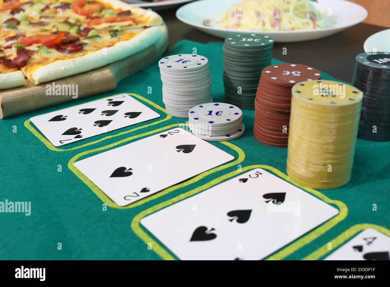 Giocare a carte e patatine su un tavolo verde vicino a una pizza su un piatto e pasta Foto Stock