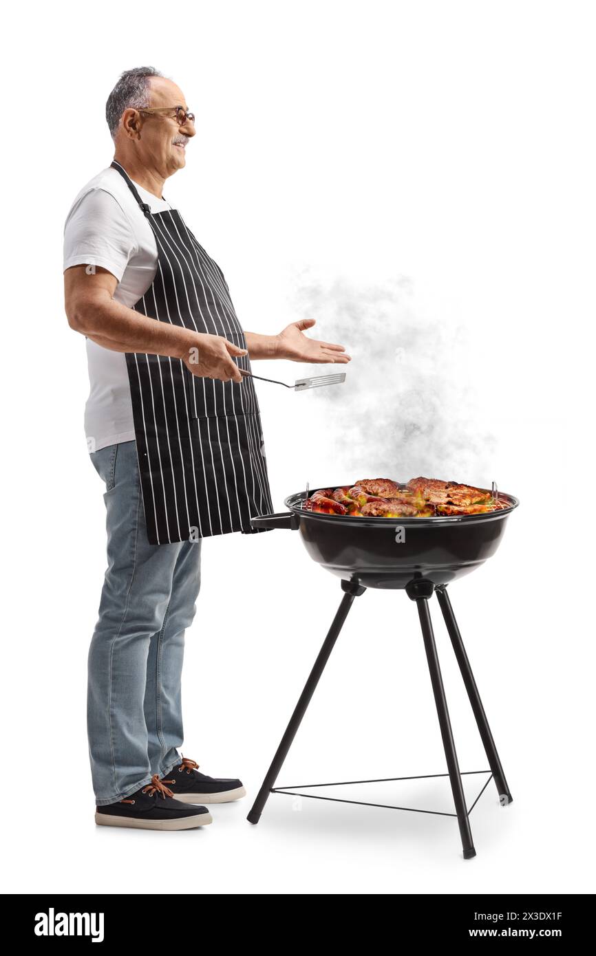 Uomo maturo che indossa grembiule e carne alla griglia su un barbecue isolato su sfondo bianco Foto Stock