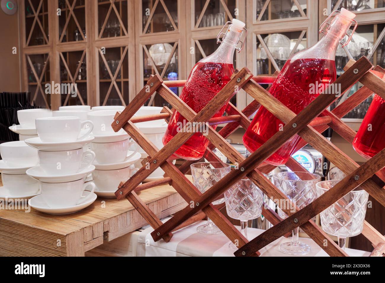 Bottiglie con bevanda rossa, bicchieri da vino e tazze su un tavolo di legno. Foto Stock