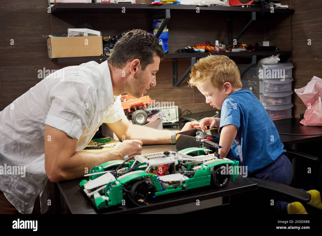 Padre e figlio piccolo costruiscono modelli di auto sul tavolo in garage. Foto Stock