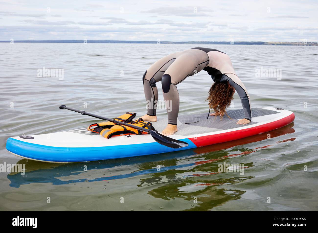 La donna con la tuta da surfista sta in posizione granchio sulla tavola gonfiabile SUP sull'acqua. Foto Stock