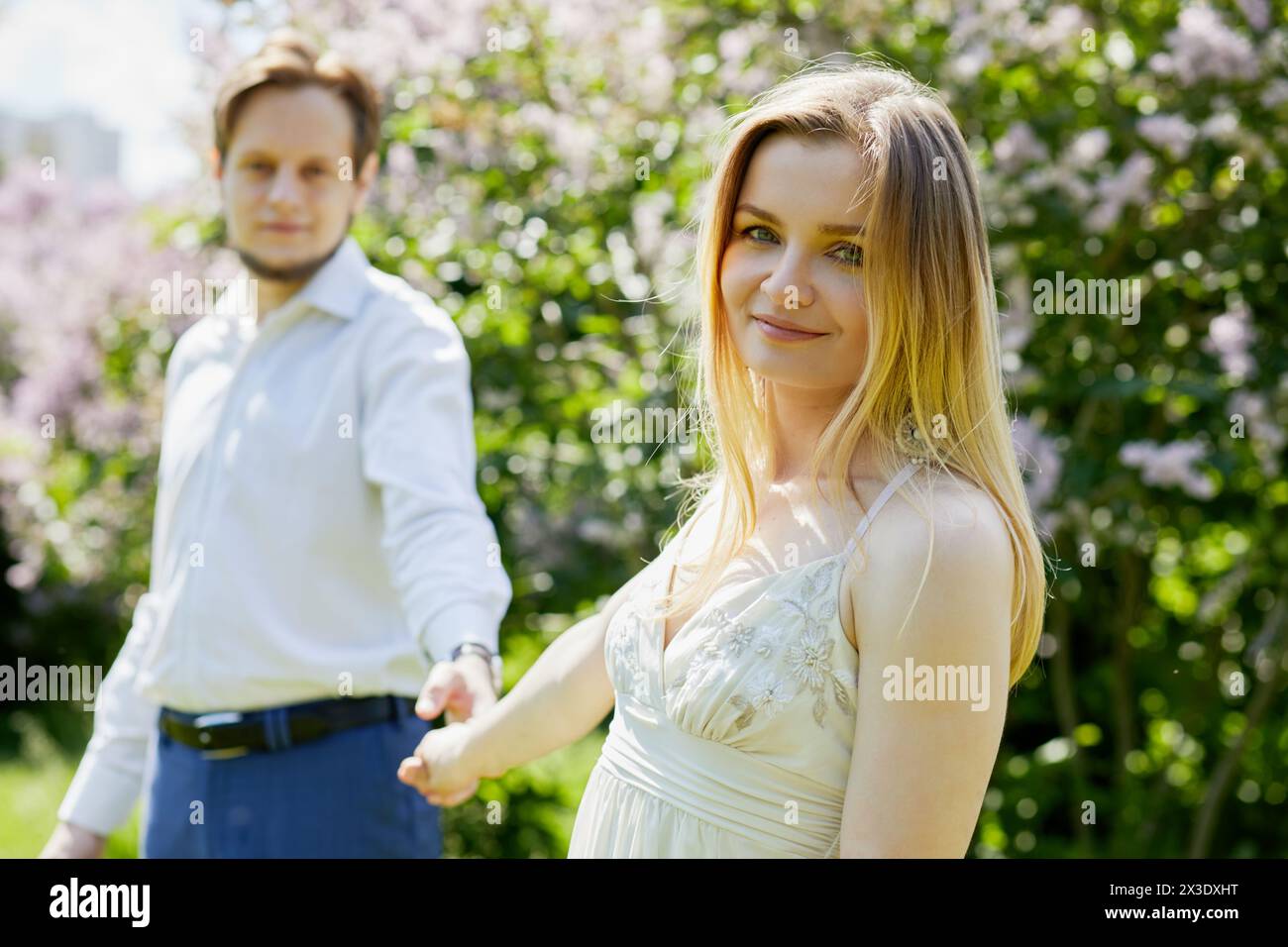 La giovane donna sorridente e l'uomo barbuto stanno tenendo le mani nel parco, concentrati sulla donna. Foto Stock