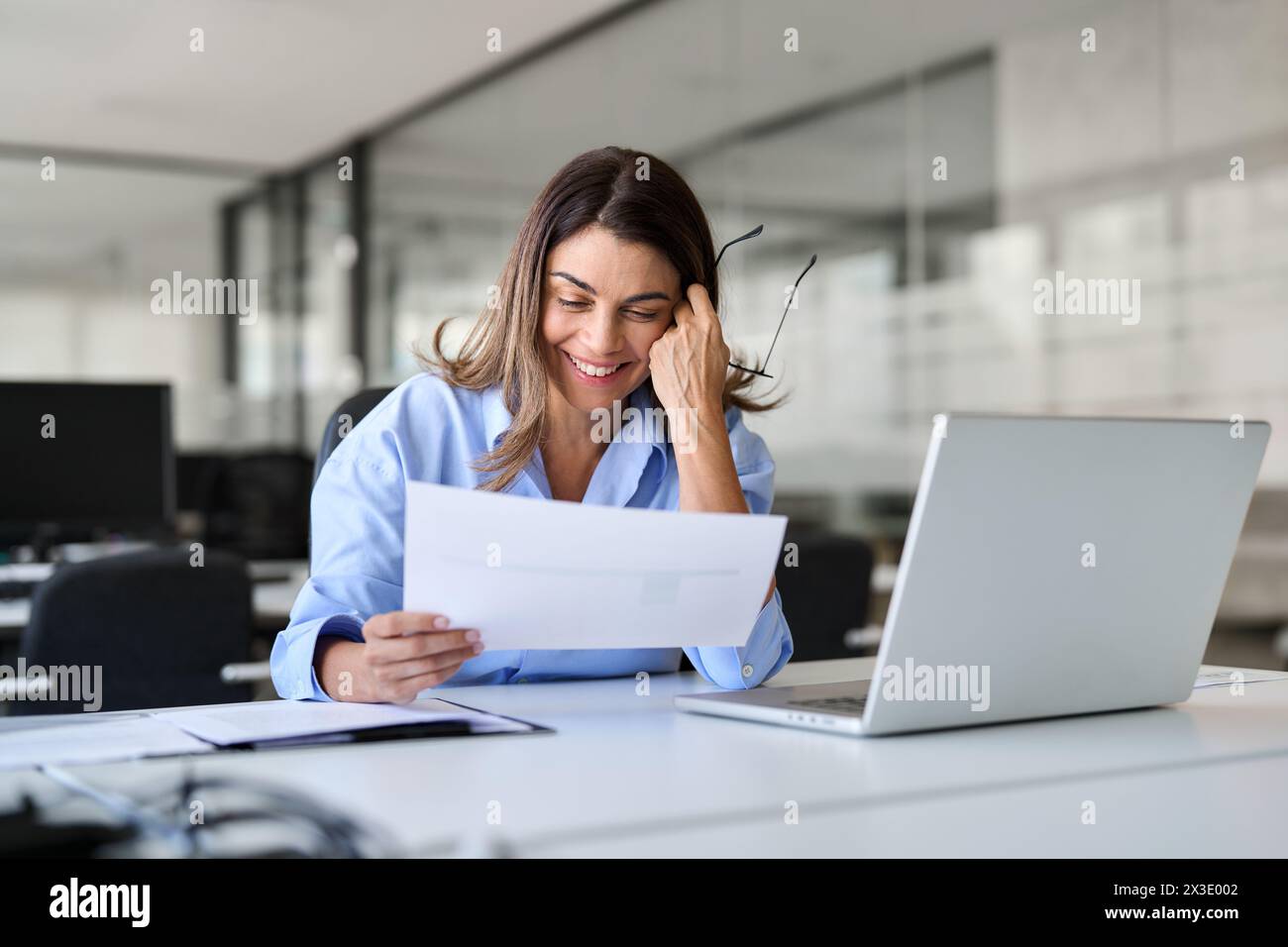 Donna d'affari di mezza età felice e impegnata che lavora in ufficio leggendo un documento. Foto Stock