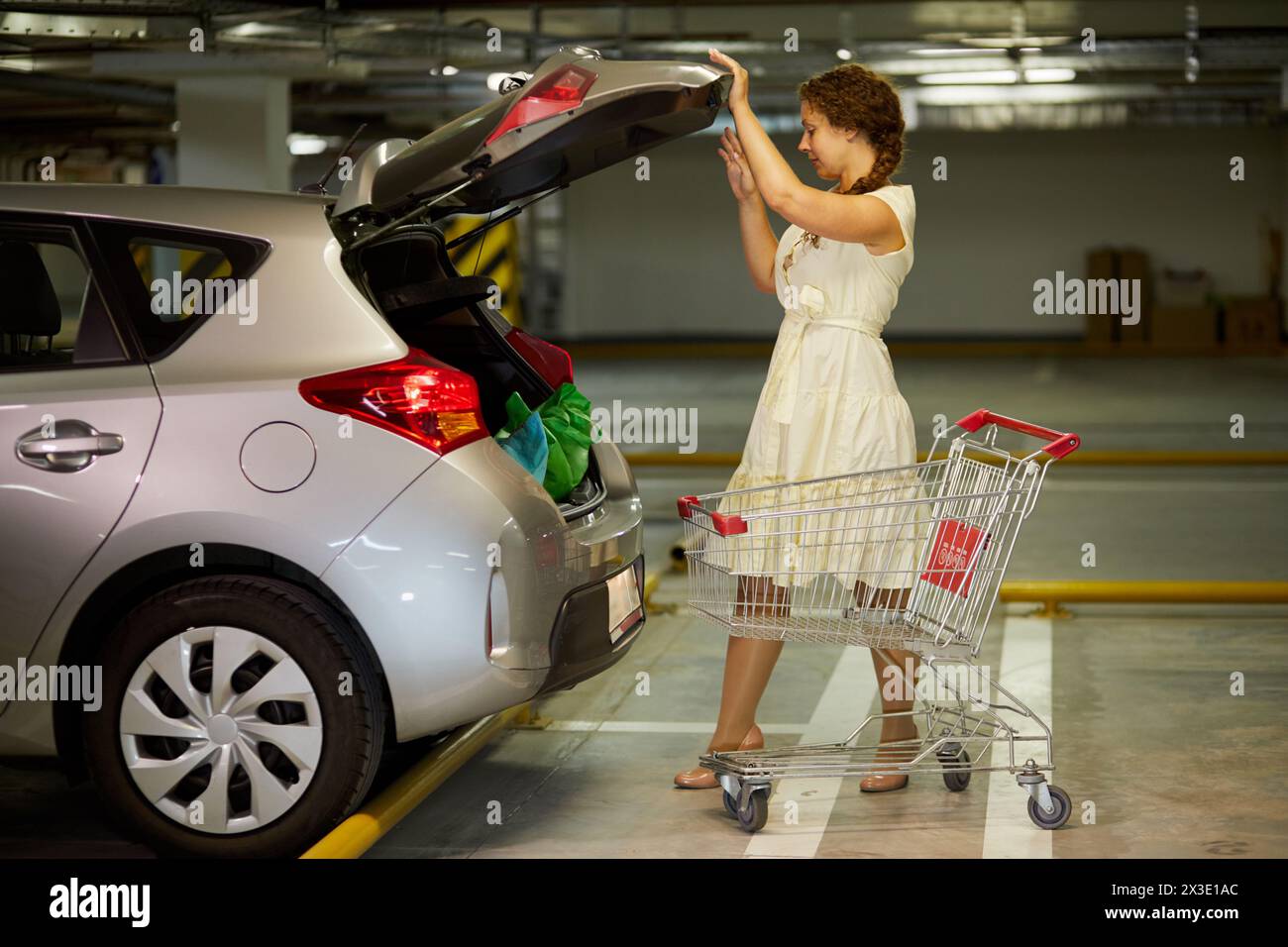 Una giovane donna chiude la porta del bagagliaio dell'auto nel parcheggio sotterraneo. Foto Stock