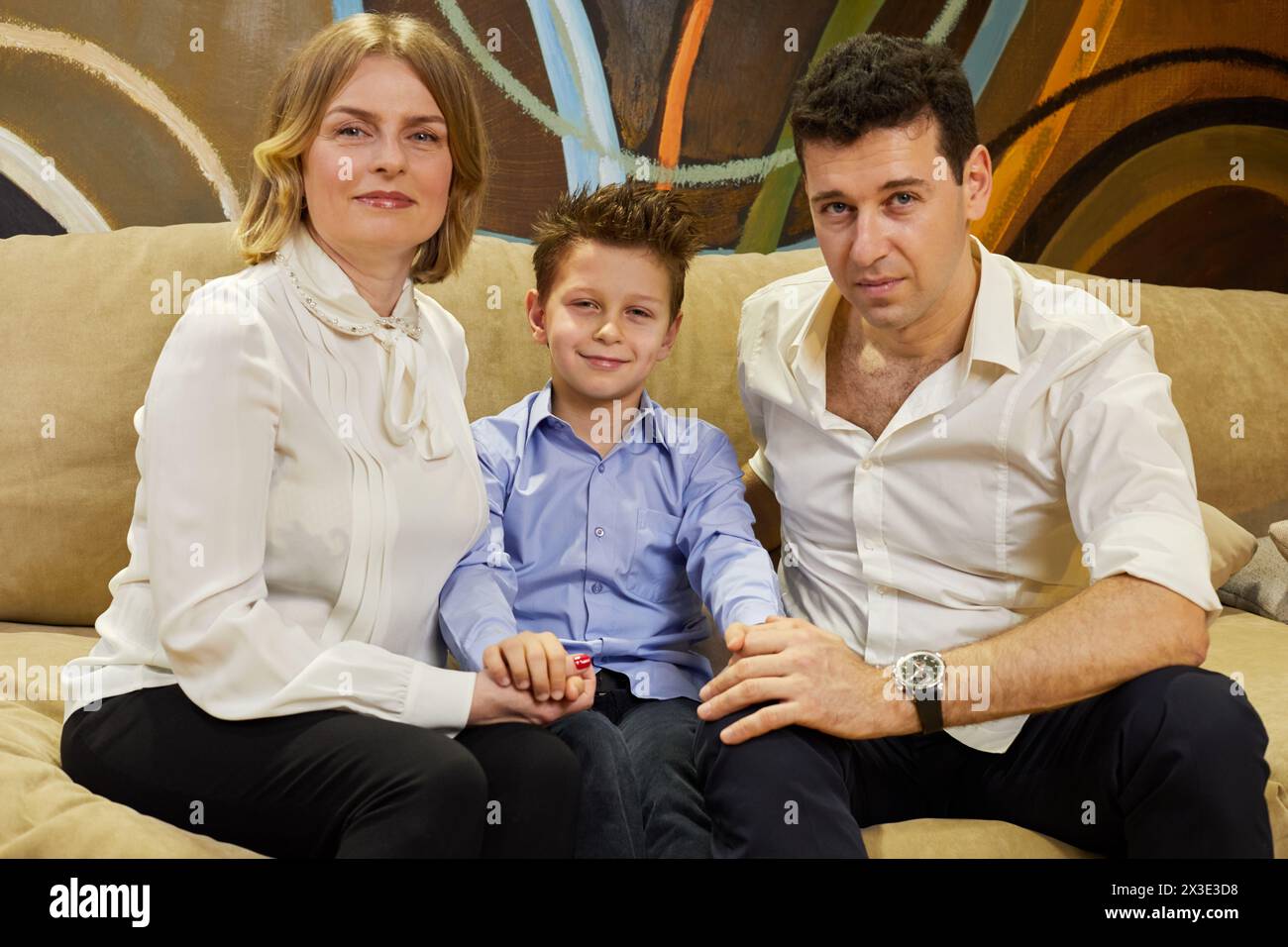 Una famiglia di tre persone siede tenendo le mani sul divano in camera. Foto Stock