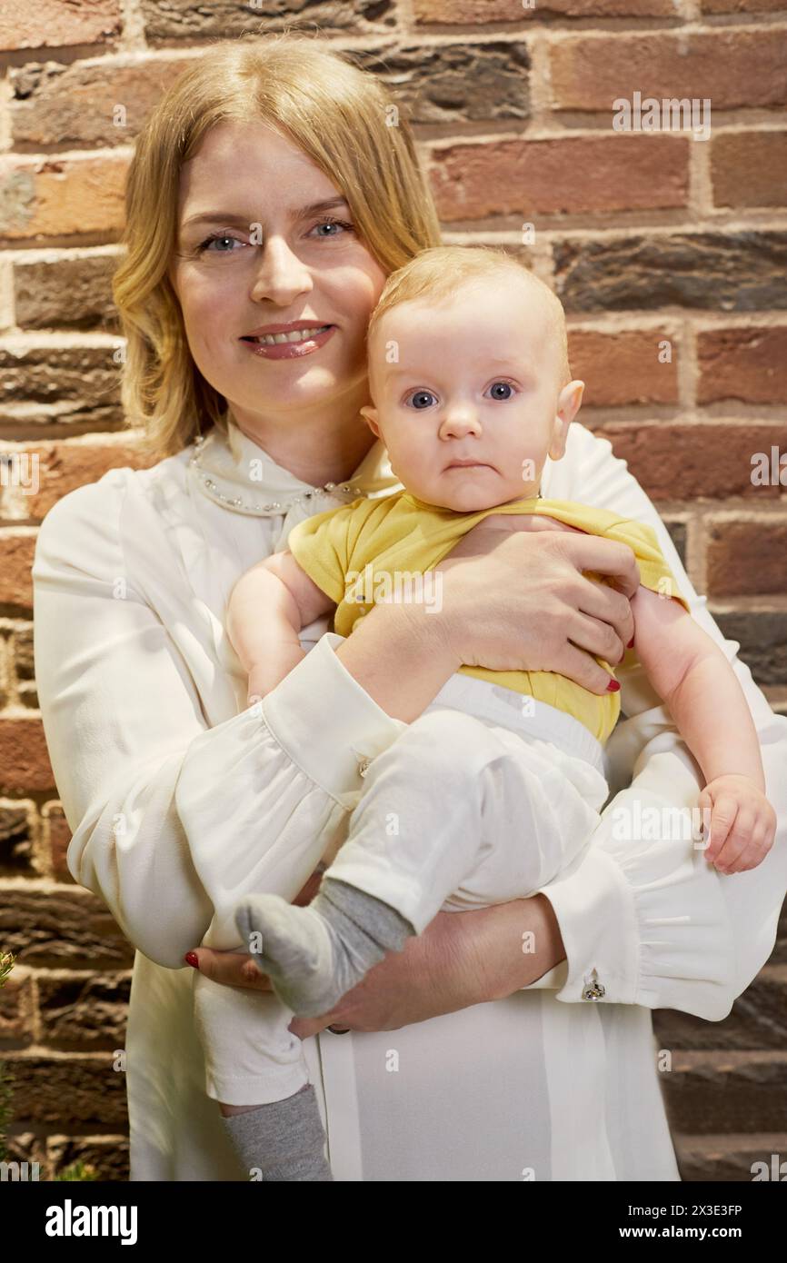 Donna sorridente con il bambino in braccio contro una parete di mattoni rossi al chiuso. Foto Stock