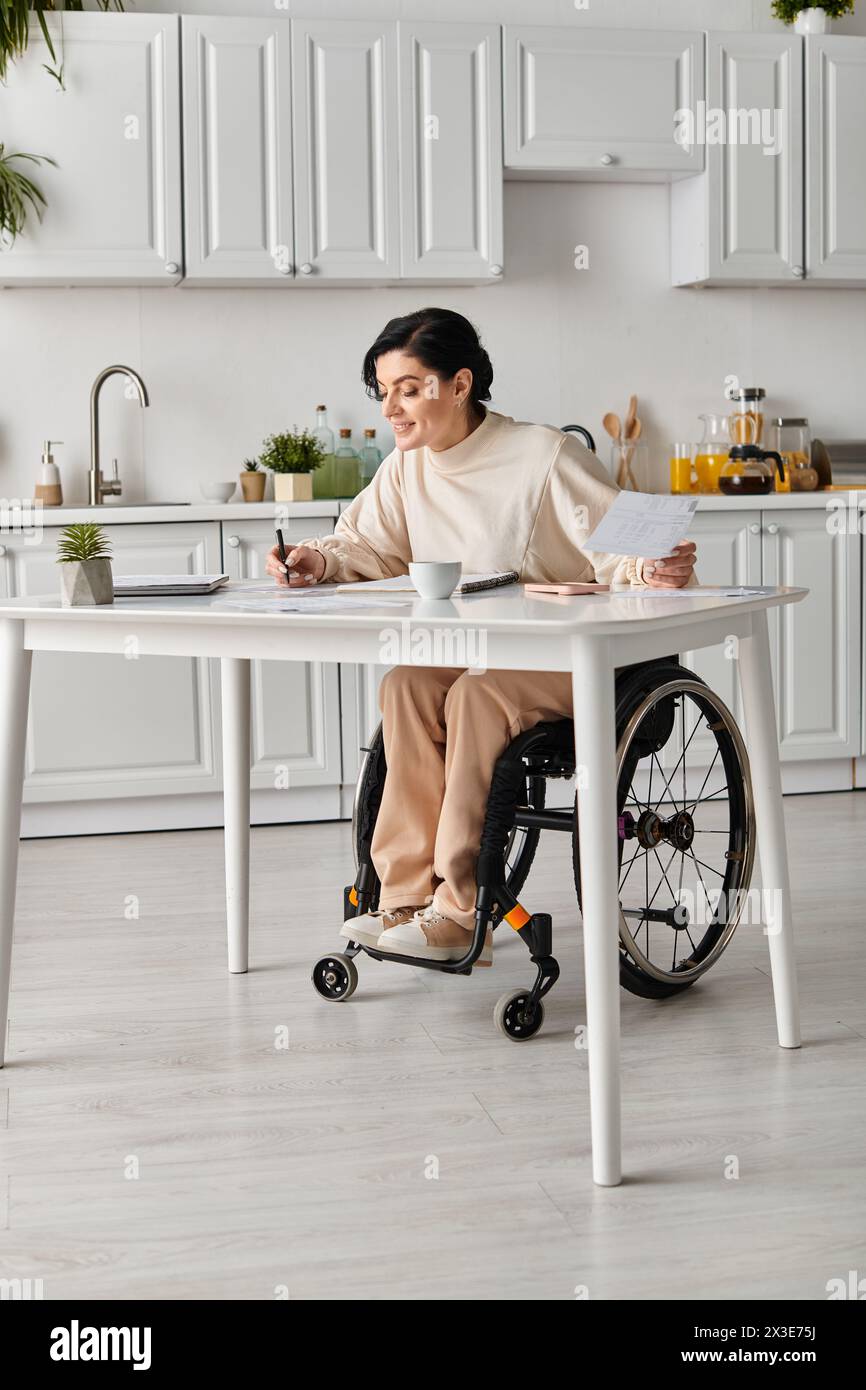 Una donna disabile in sedia a rotelle lavora al tavolo della cucina. Foto Stock