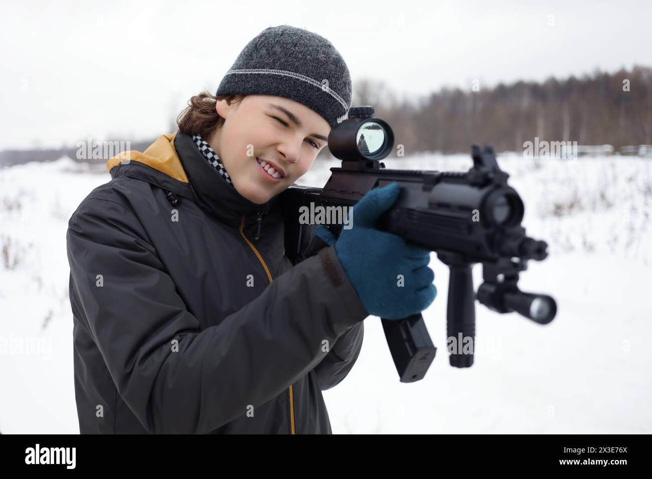 Adolescente felice con la pistola prende la mira durante la partita laser all'aperto in inverno Foto Stock