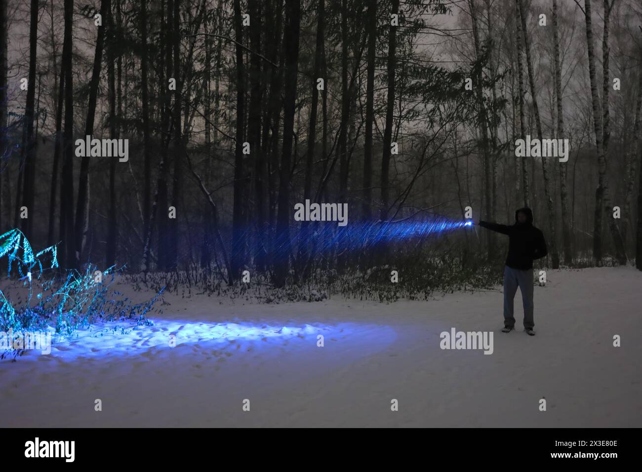 L'uomo con torcia elettrica si trova nella foresta notturna buia durante la tormenta d'inverno Foto Stock