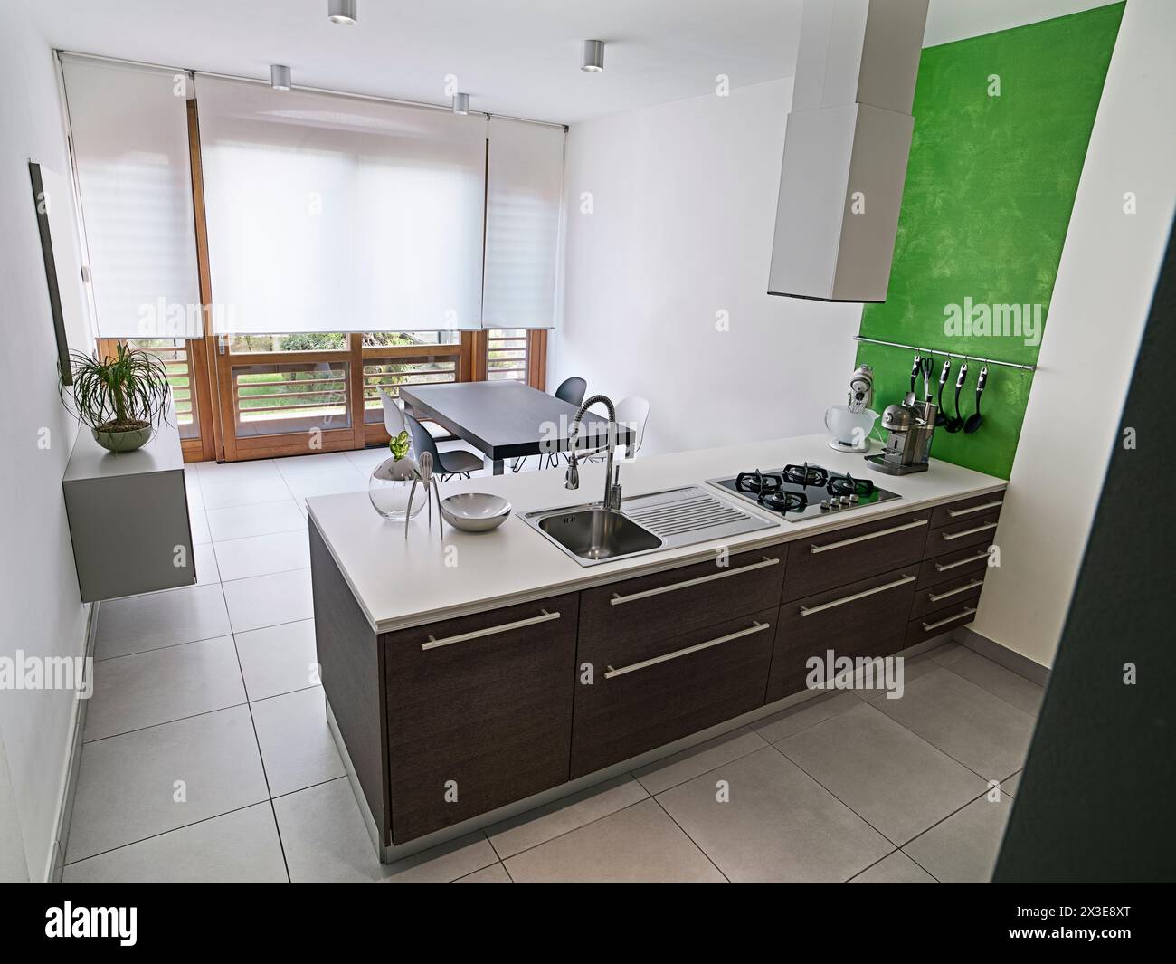 vista interna di una cucina moderna in primo piano c'è una cucina isolana e sullo sfondo c'è un tavolo da pranzo vicino alla porta francese Foto Stock