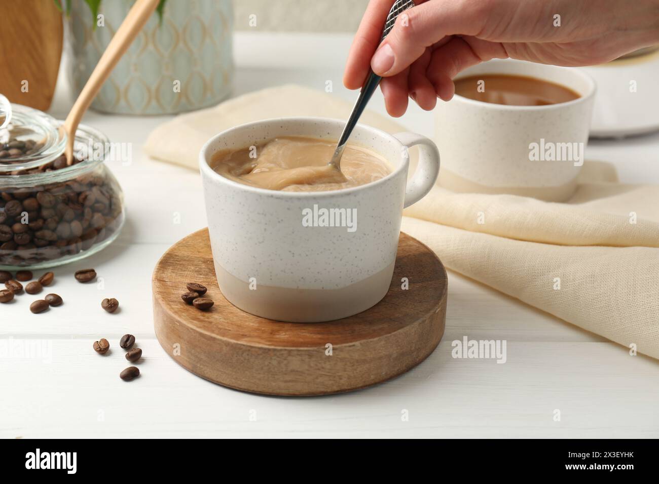 Donna che mescola il caffè con un cucchiaio al tavolo di legno bianco, primo piano Foto Stock