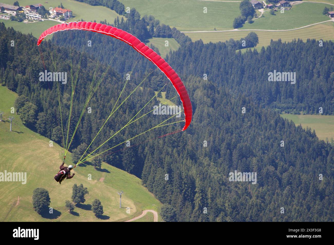 Un parapendio rosso sorvola prati e boschi circostanti. Foto Stock