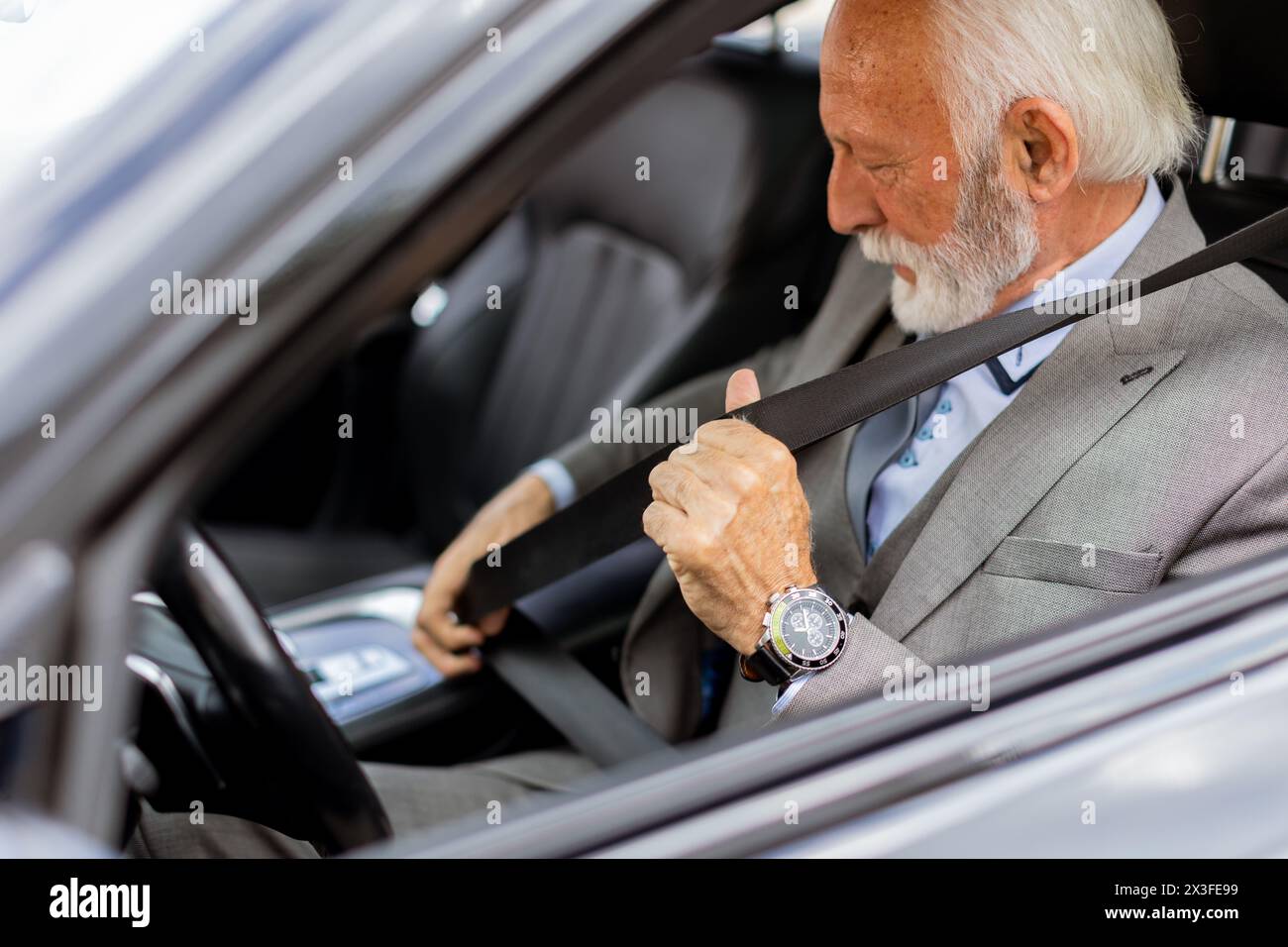 Uomo anziano sofisticato con un abito che indossa la cintura di sicurezza, pronto per un viaggio Foto Stock