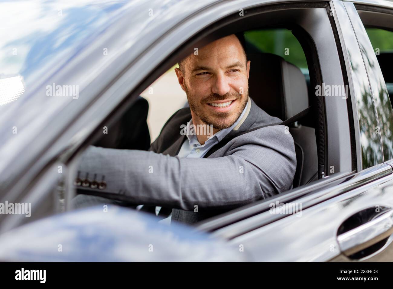 Il conducente sorride mentre tiene il volante, guidando lungo la strada in un veicolo ben equipaggiato Foto Stock