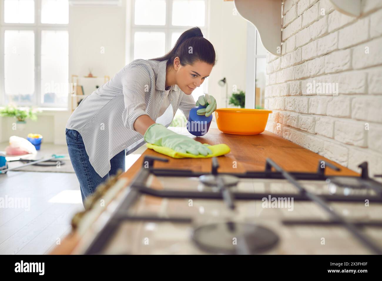 Sorridente casalinga che spaying detergente di pulizia sulla superficie del contatore della cucina e pulirlo con un panno morbido Foto Stock