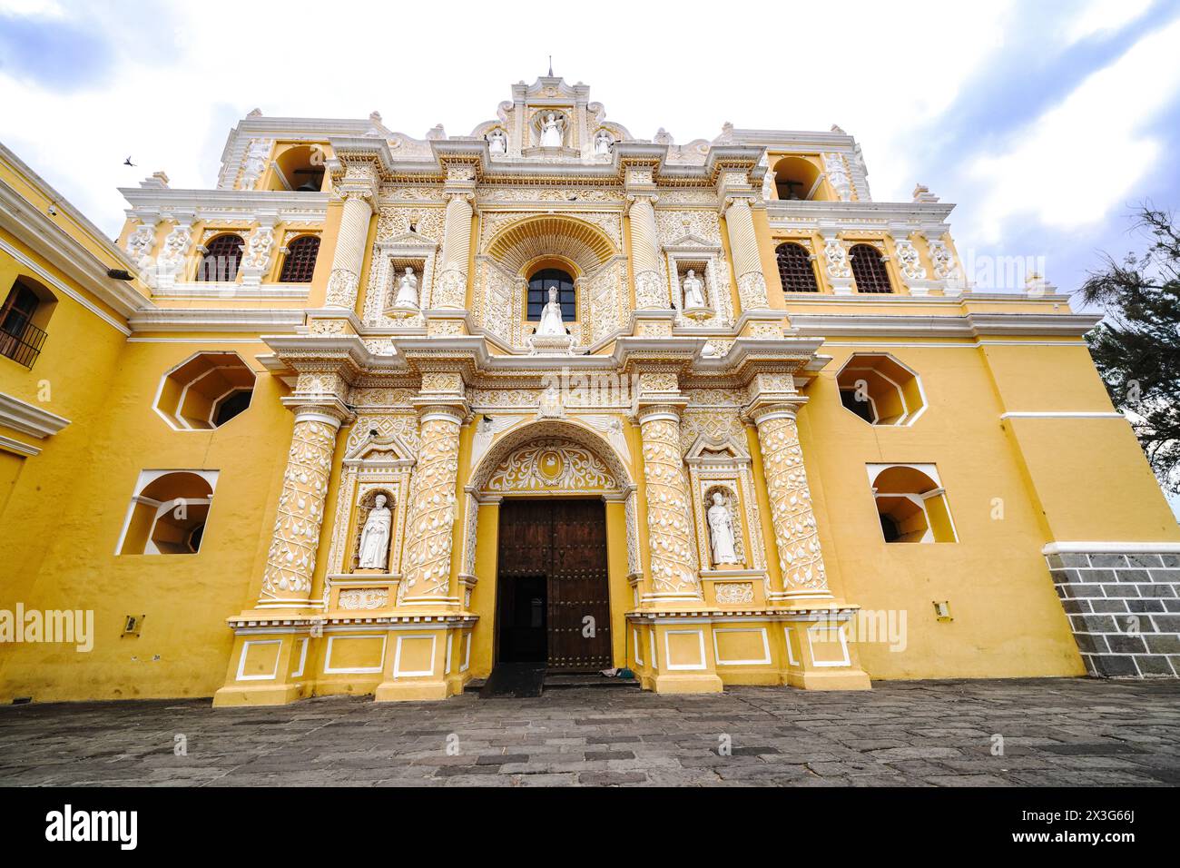 Facciata esterna della Chiesa e del Convento di la Merced, una chiesa cattolica ornata costruita in stile churrigueresco nel 1749 ad Antigua, Guatemala. L'edificio ornato di giallo luminoso presenta dettagli a rilievo in motivi arabeschi chiamati stucco Ataurique. Foto Stock