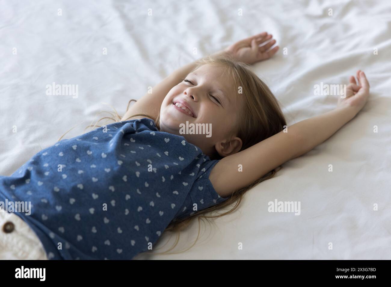 La bambina si diverte a riposare sdraiata su lenzuola bianche Foto Stock