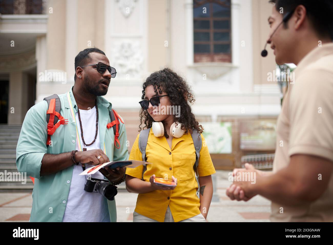 Giovane turista maschile con una brochure in mano che parla con la guida durante l'escursione mentre gli fa domande sulle visite turistiche Foto Stock