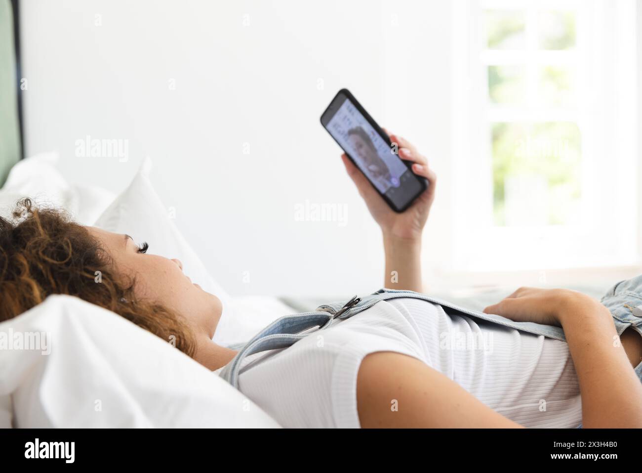 Giovane donna caucasica sdraiata a casa a guardare lo smartphone Foto Stock