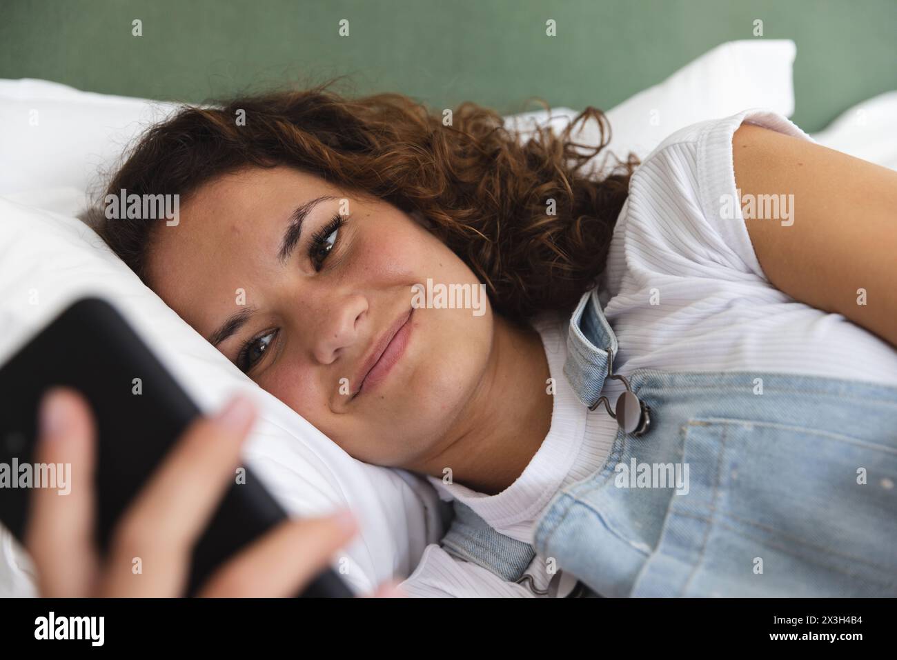 Una giovane donna caucasica che tiene lo smartphone, sdraiata a casa Foto Stock