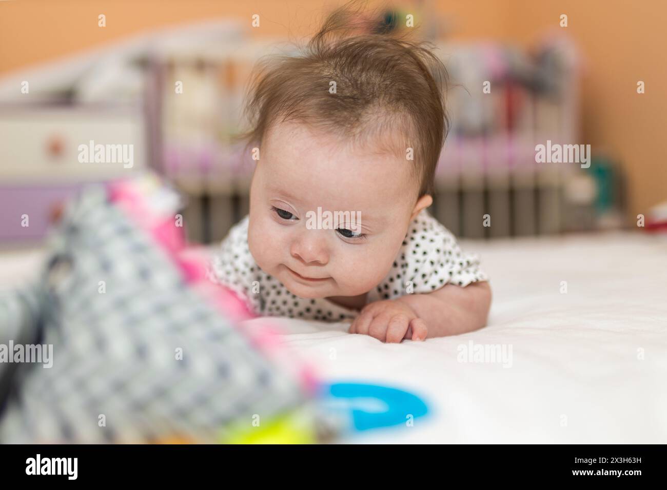 Bambina con la sindrome di Down stai in piedi sulla pancia e guarda un giocattolo Foto Stock