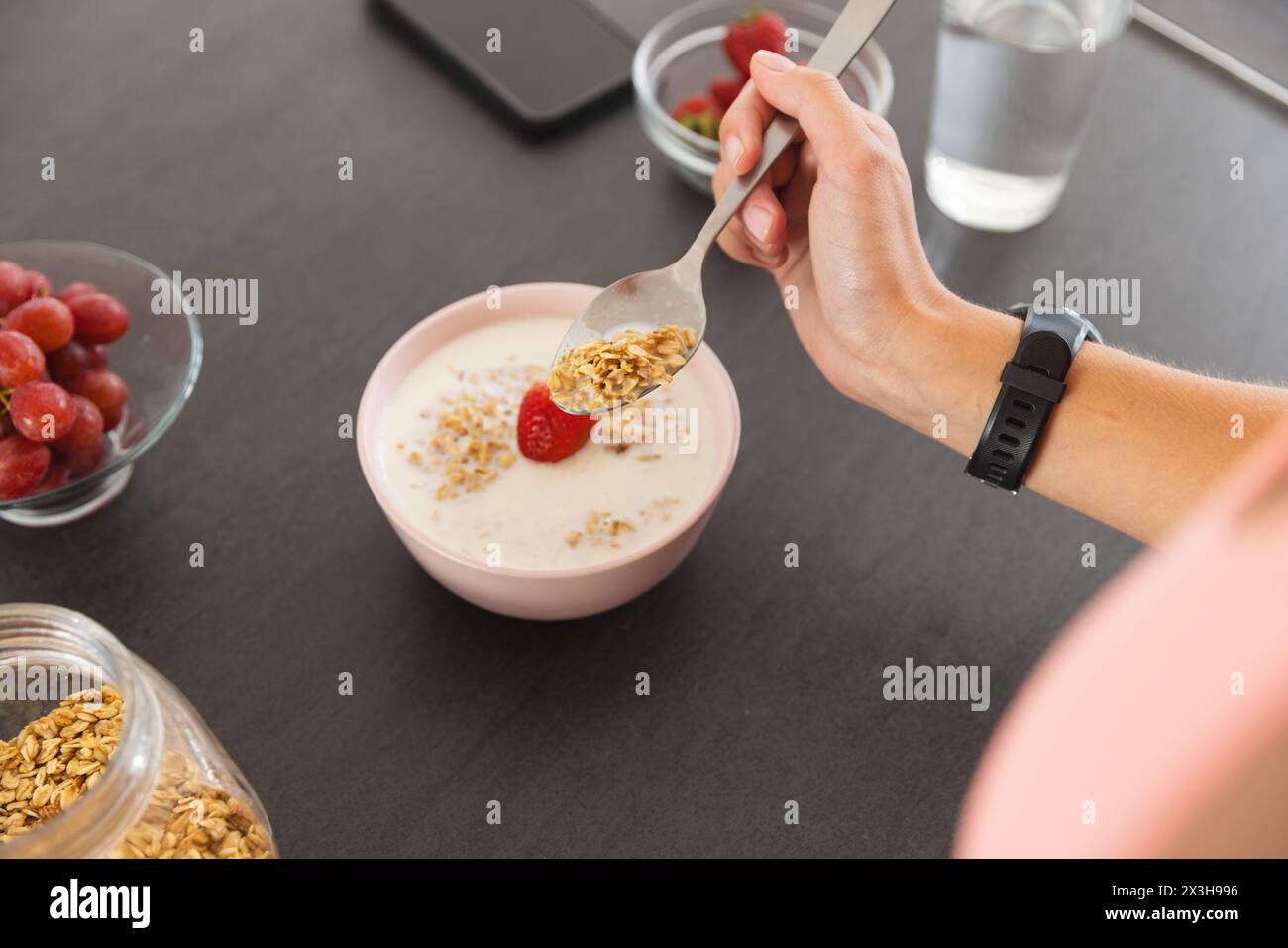 Una giovane donna caucasica che indossa un fitness tracker che fa colazione a casa Foto Stock