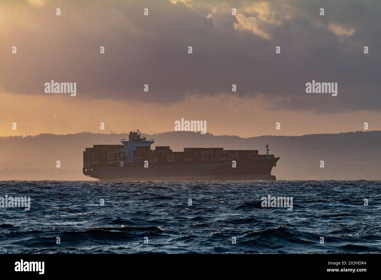 Nave portacontainer MSC Pratiti in silhouette sul lato gallese dell'estuario del Severn prelevata dalla spiaggia di Clevedon Foto Stock