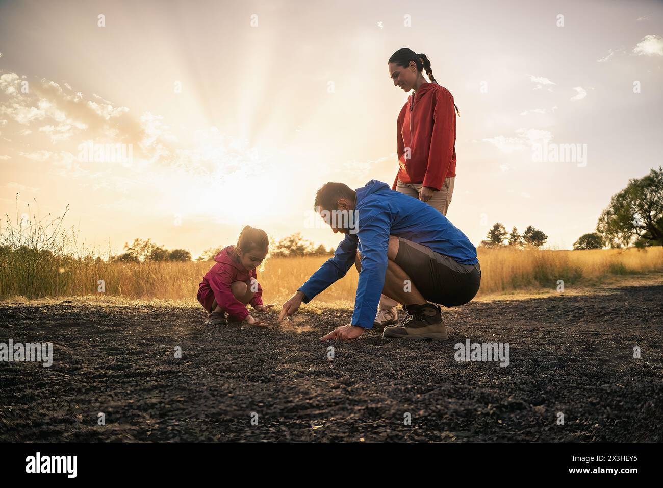 Famiglia che esplora la natura al crepuscolo - un bambino curioso con i genitori - esplorando, imparando e legandosi nel calore di un tramonto. Foto Stock