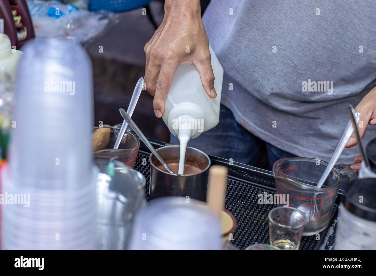 Il commerciante maschile sta versando il latte in una bottiglia con caffè per mescolarlo in un menu di caffè a latte freddo, il caffè a latte freddo è una bevanda popolare in Thailandia, Blurre Foto Stock