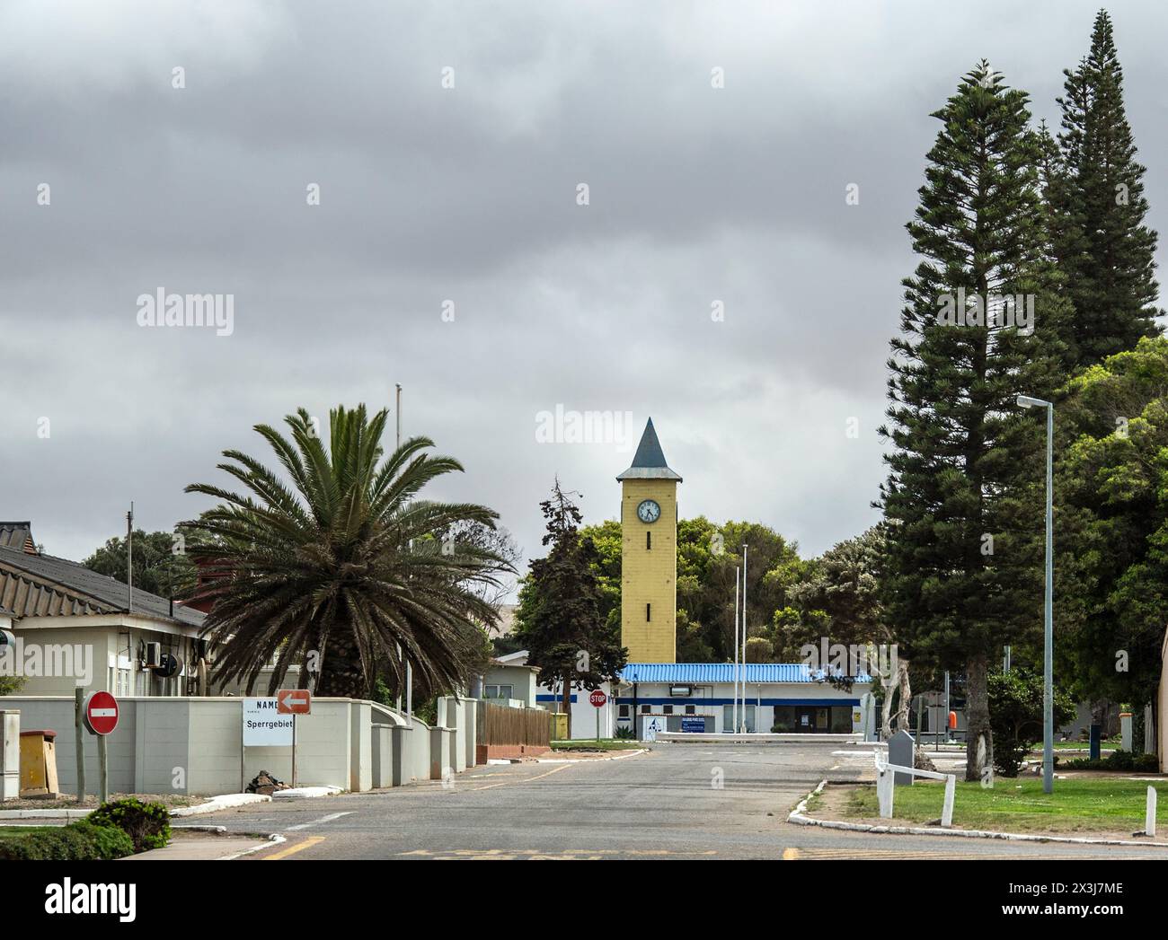La torre dell'orologio gialla della scuola privata di Oranjemund, blu e bianca, alla fine di un'ampia e verde strada di Oranjemund. Foto Stock