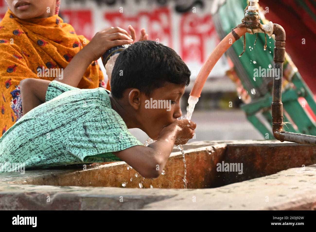 Un bambino sta bevendo acqua da un gasdotto lungo la strada durante le ondate di caldo a Dacca, Bangladesh, il 27 aprile 2024 credito: Mamunur Rashid/Alamy Live News Foto Stock
