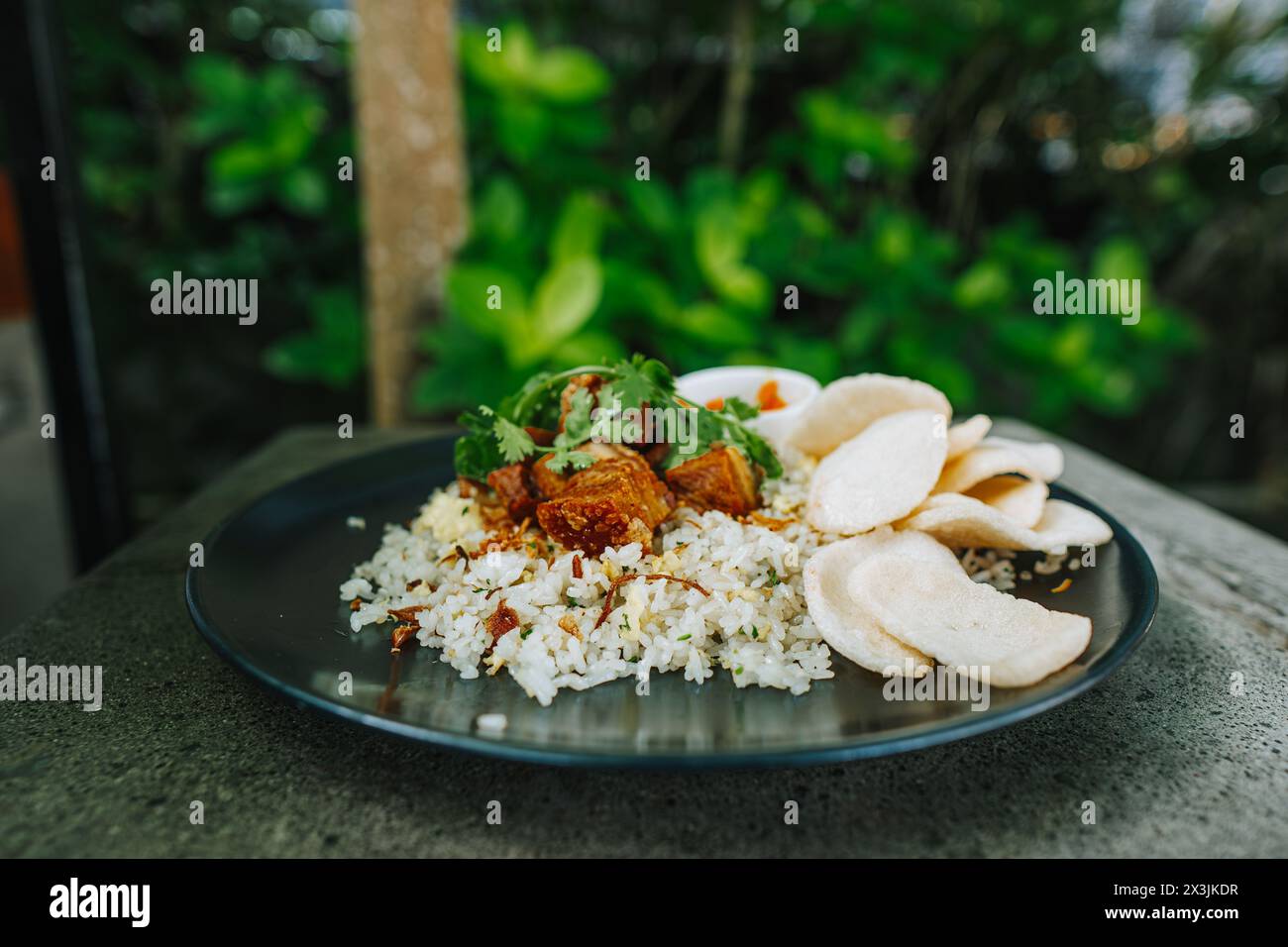 Nasi Goreng con carne di maiale, verdure, peperoncino e cracker in un piatto nero sul tavolo di pietra Foto Stock