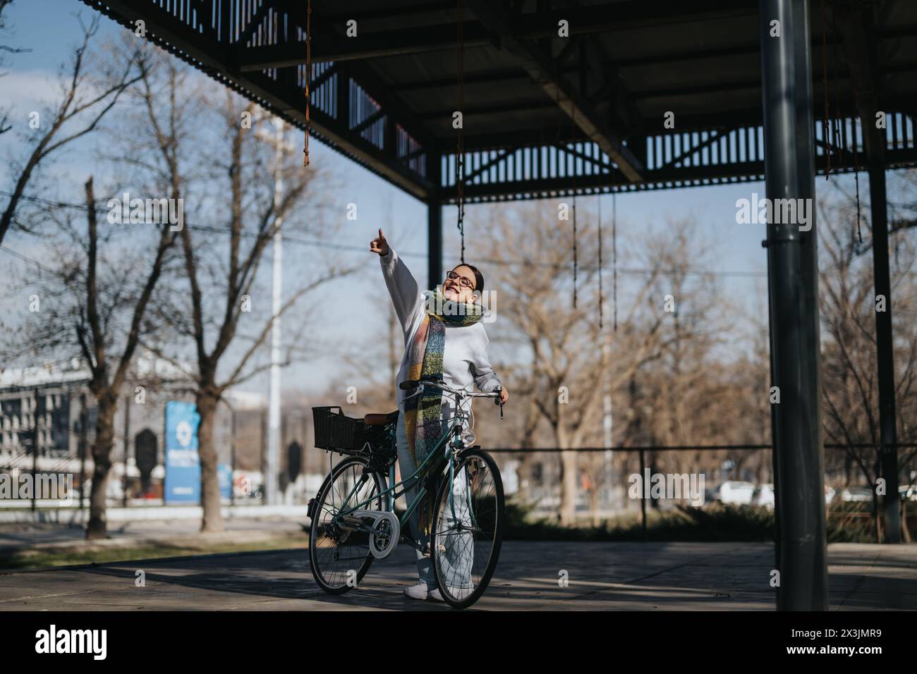 Donna anziana gioiosa con bicicletta rivolta verso l'alto in un parco urbano. Foto Stock