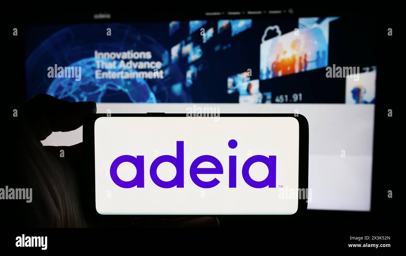 Persona che detiene un cellulare con il logo della società statunitense Adeia Inc. Di fronte alla pagina Web aziendale. Mettere a fuoco il display del telefono. Foto Stock