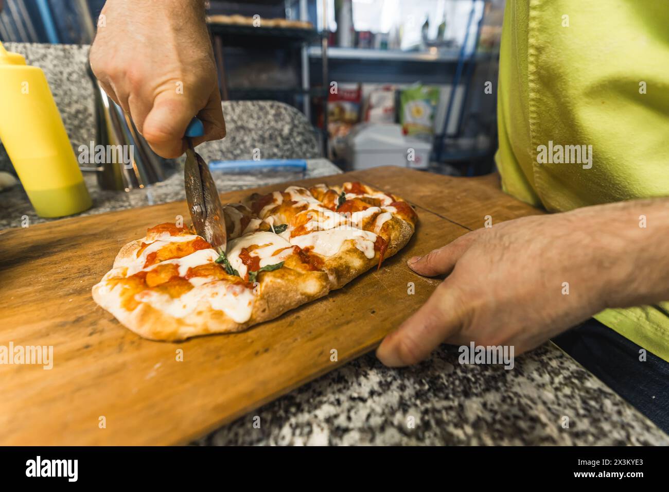 chef in uniforme verde insalata che affetta pizza alla panetteria. Foto di alta qualità Foto Stock
