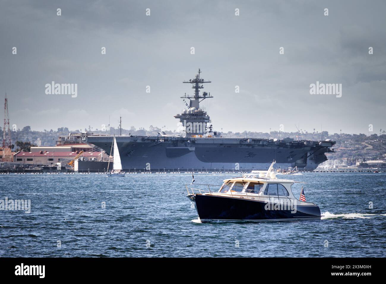 Una barca sull'acqua, con una portaerei della US Navy sullo sfondo, nella baia di San Diego al largo della costa di Coronado, California. Foto Stock