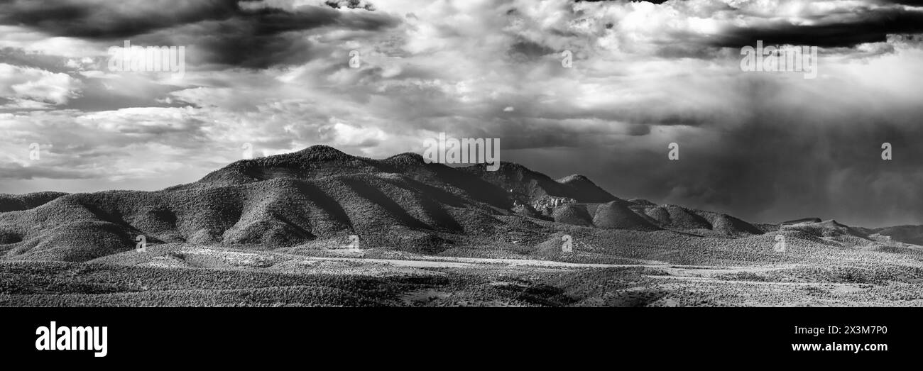 Una catena montuosa lontana vicino a Glenwood, NEW MEXICO. Una piccola formazione di rocce bianche affilate appare proprio a destra del centro del telaio. Molte nuvole e deserto Foto Stock