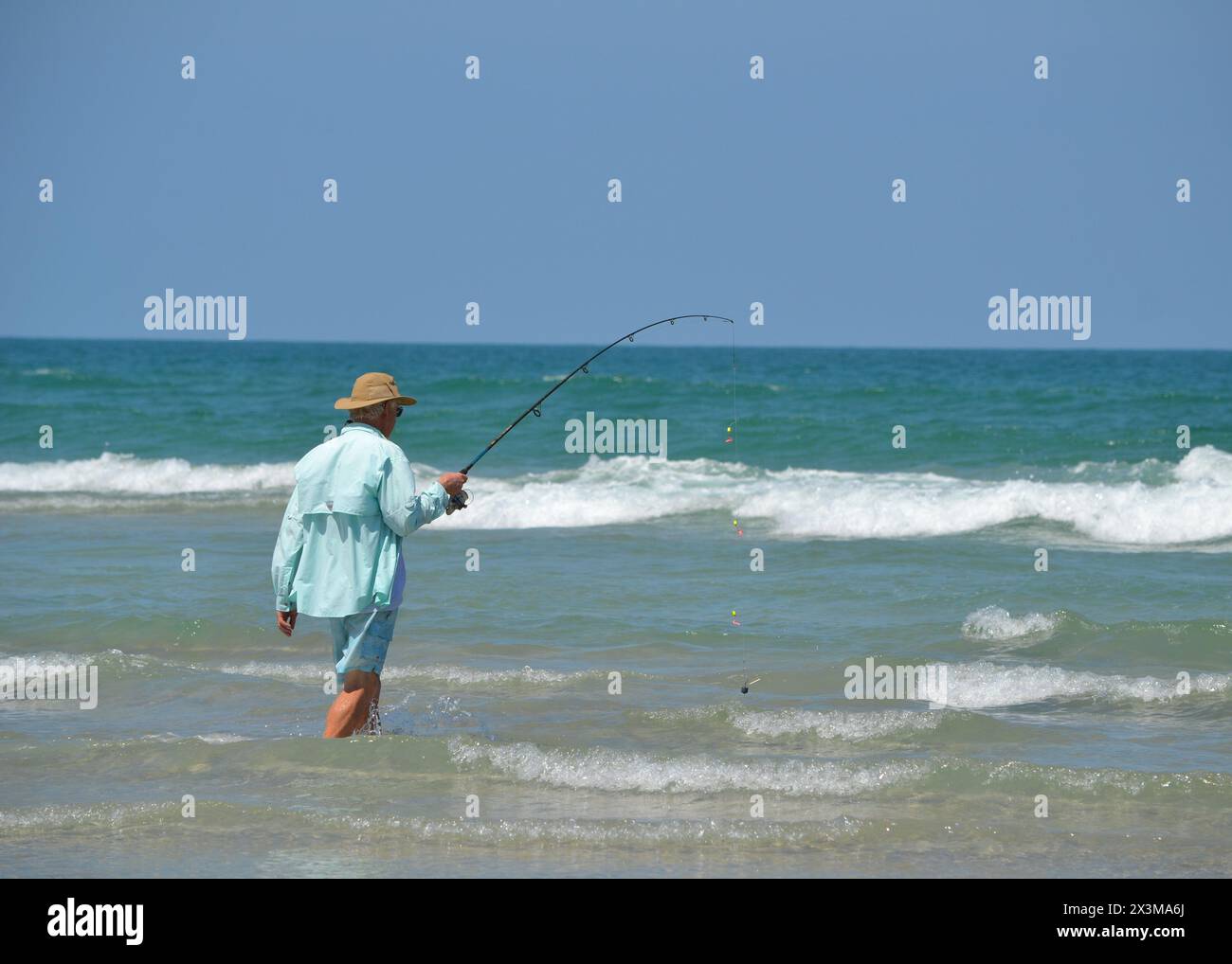 Sull'orlo dell'oceano, un pescatore da surf si immerge nelle acque di Ponce Inlet, Jetty Beach in Florida, stringendo la sua canna da pesca. Foto Stock