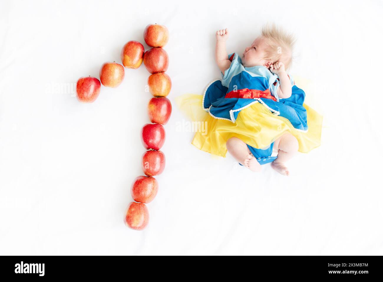 Immagine piatta di un bambino di 1 mese con un numero di mele fatte. Bambina appena nata in un abito da principessa. Costume da favola su un bambino. 1 mese con n Foto Stock