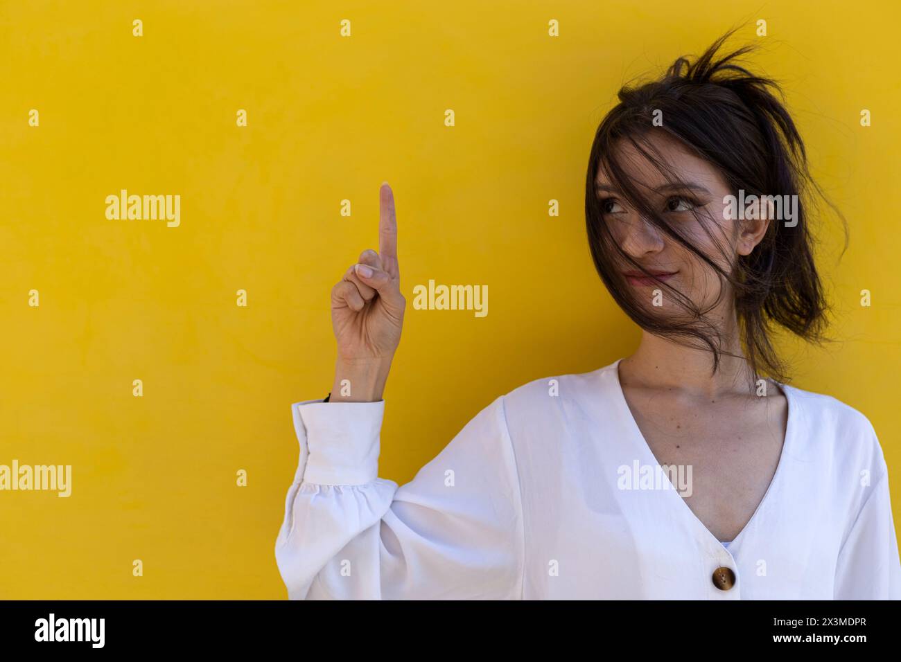 Ritratto di una giovane donna latinoamericana sorridente (24) isolata su sfondo giallo punta con un dito della mano a svuotare lo spazio superiore. Concept pro Foto Stock