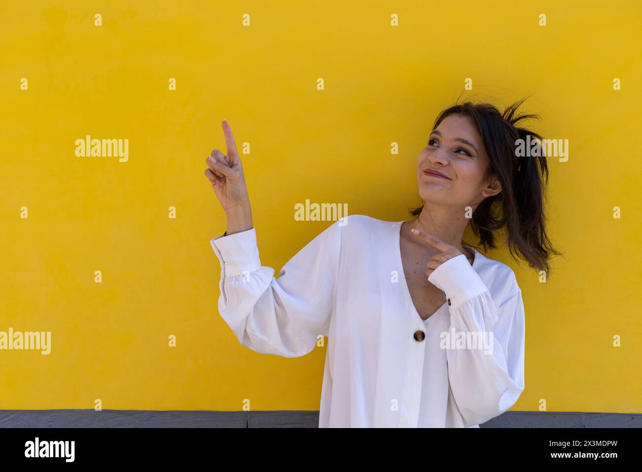 Ritratto di una giovane donna latinoamericana sorridente (24) isolata su sfondo giallo punta con entrambe le dita della mano a uno spazio vuoto. Promo concettuale Foto Stock