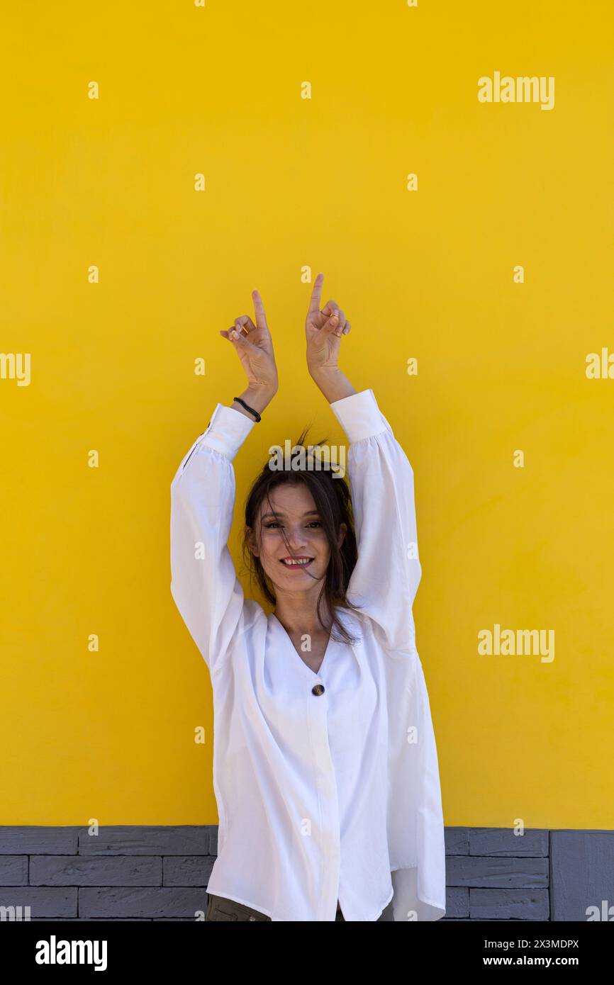 Ritratto di una giovane donna latinoamericana sorridente (24) isolata su sfondo giallo punta con entrambe le dita della mano a uno spazio vuoto. Promo concettuale Foto Stock