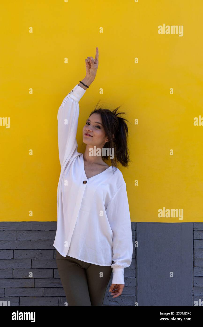 Ritratto di una giovane donna latinoamericana sorridente (24) isolata su sfondo giallo punta con un dito della mano a svuotare lo spazio superiore. Concept pro Foto Stock
