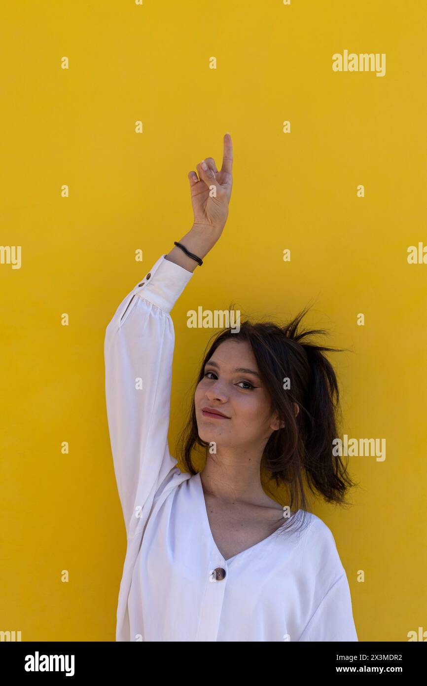 Ritratto di una giovane donna latinoamericana sorridente (24) isolata su sfondo giallo punta con un dito della mano a svuotare lo spazio superiore. Concept pro Foto Stock