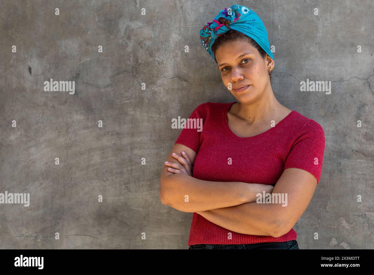 Ritratto di donna (34) afro latino-americana con sciarpa sulla testa, isolata su sfondo grigio con le braccia incrociate guarda la fotocamera. Copia spazio. Conc Foto Stock