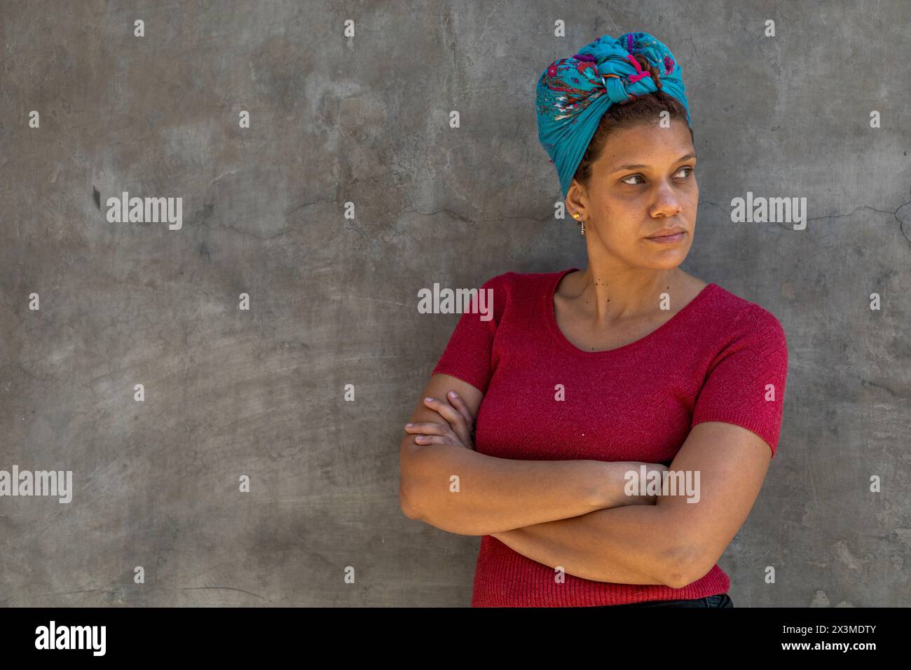 Ritratto di donna (34) afro latinoamericana con sciarpa sulla testa, isolata su sfondo grigio con le braccia incrociate guarda alla sua sinistra. Copia spac Foto Stock