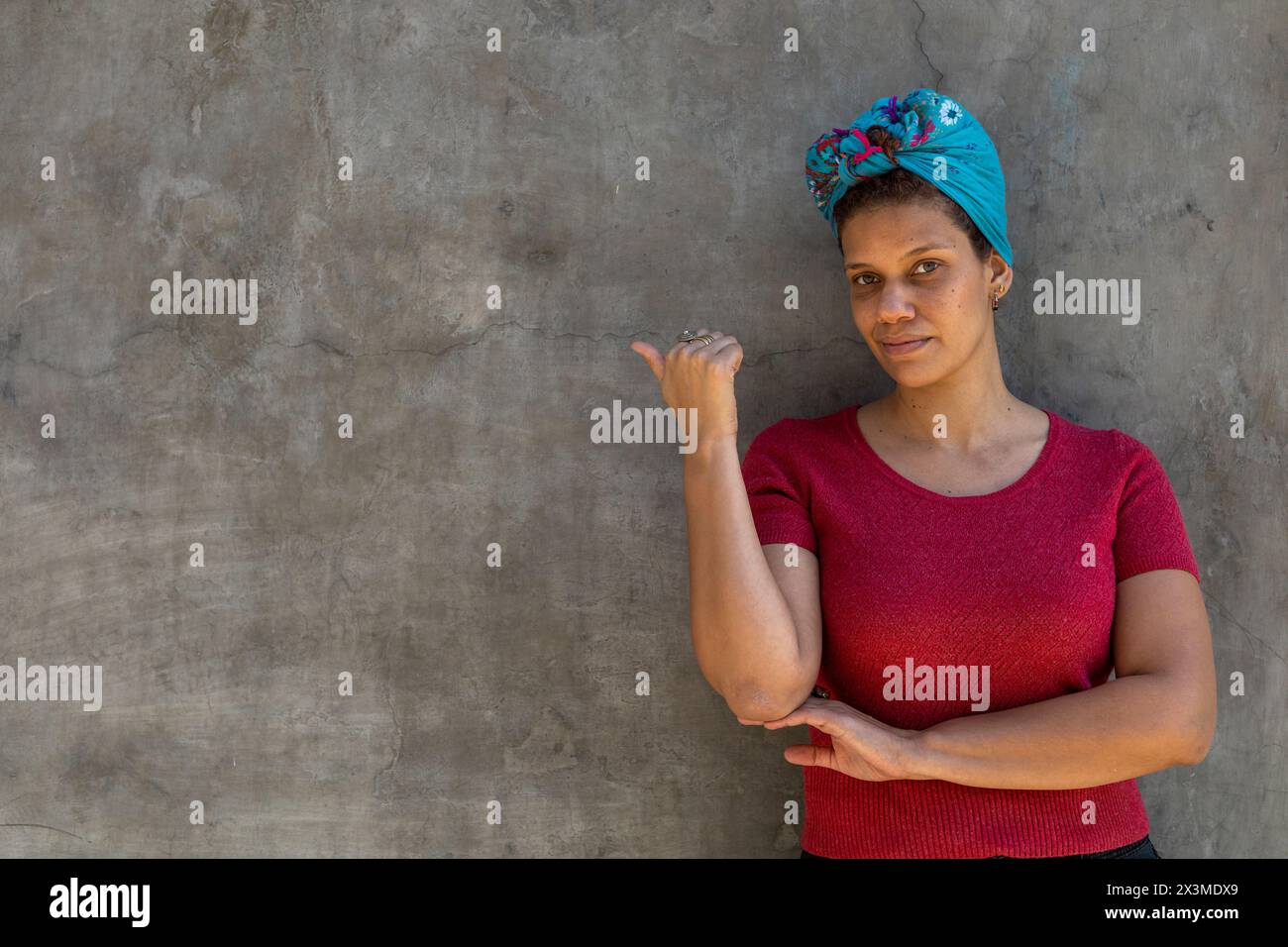 Ritratto di donna latinoamericana sorridente (34) di discendenza africana con foulard, isolato su sfondo grigio punta con pollice verso uno spazio vuoto. Conc Foto Stock