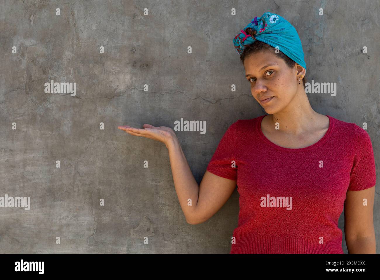 Ritratto di donna latinoamericana (34) di discendenza africana con sciarpa sulla testa, isolata su sfondo grigio punta con il palmo aperto della mano a. Foto Stock