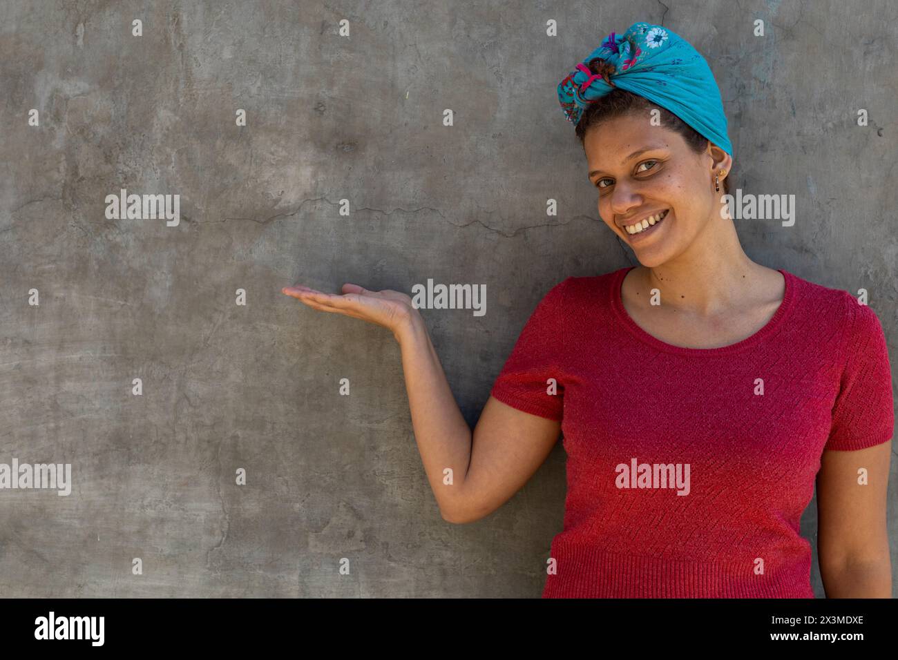 Ritratto di donna latinoamericana (34) di discendenza africana con sciarpa sulla testa, isolata su sfondo grigio punta con il palmo aperto della mano a. Foto Stock
