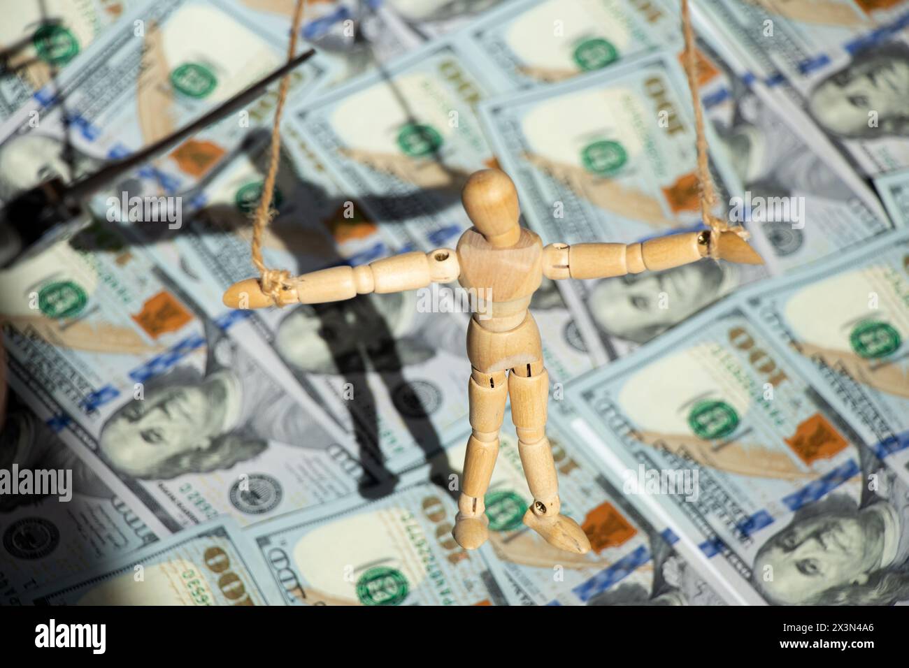 Una bambola di legno pesa su una corda contro uno sfondo di dollari e manipola le persone con soldi Foto Stock